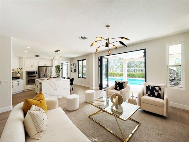 living area featuring baseboards, light wood-style floors, a notable chandelier, and visible vents