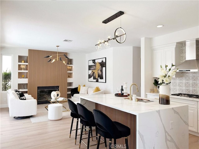 kitchen featuring a sink, stainless steel gas stovetop, wall chimney exhaust hood, and an inviting chandelier