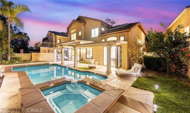 back of property at dusk with a patio area, a pool with connected hot tub, stucco siding, and fence