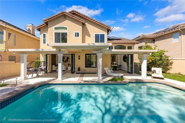 back of house with an outdoor pool, roof mounted solar panels, a patio, and stucco siding