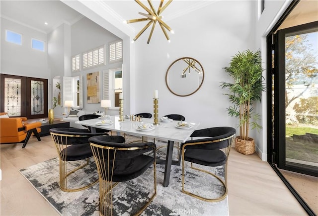 dining space featuring light wood-type flooring, plenty of natural light, a towering ceiling, and ornamental molding