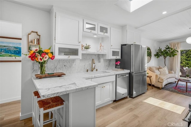 kitchen featuring stainless steel appliances, white cabinetry, a sink, and light wood-type flooring