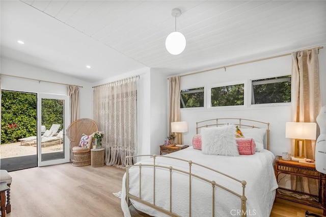 bedroom with multiple windows, lofted ceiling, wood finished floors, and access to exterior