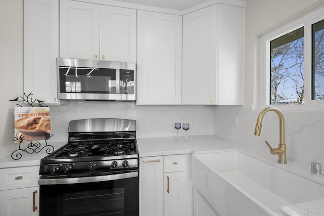 kitchen featuring stainless steel microwave, white cabinetry, black gas range, decorative backsplash, and a sink