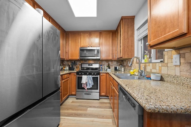 kitchen with stainless steel appliances, light wood-style floors, brown cabinets, and a sink