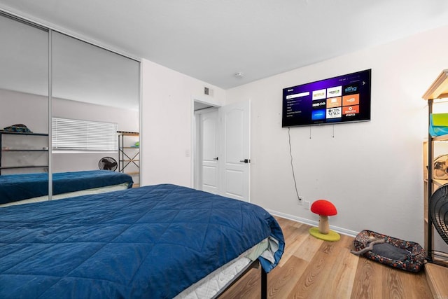bedroom with wood finished floors, baseboards, a closet, and visible vents
