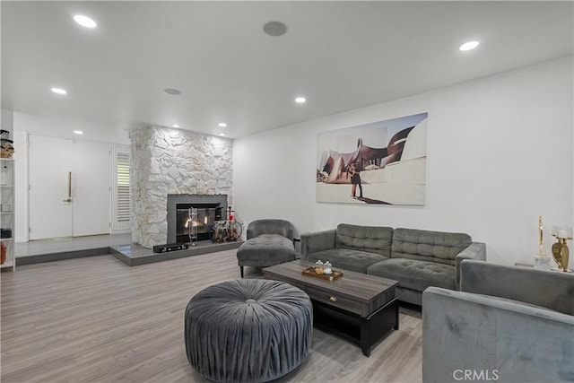 living room with recessed lighting, a stone fireplace, and wood finished floors