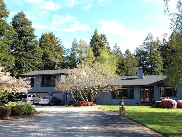tri-level home with a chimney, driveway, french doors, an attached garage, and a front lawn