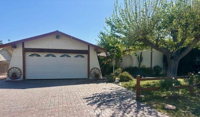single story home with a garage, stucco siding, and decorative driveway