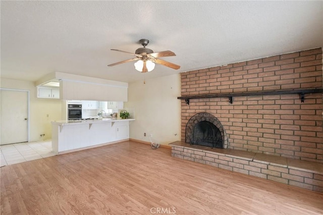unfurnished living room featuring a brick fireplace, a textured ceiling, ceiling fan, and light wood-style floors
