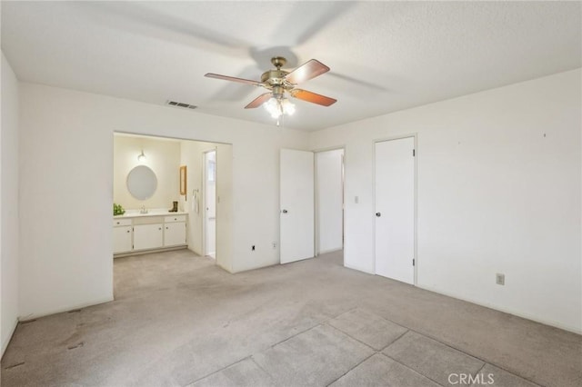 unfurnished bedroom with a sink, light colored carpet, visible vents, a ceiling fan, and ensuite bath