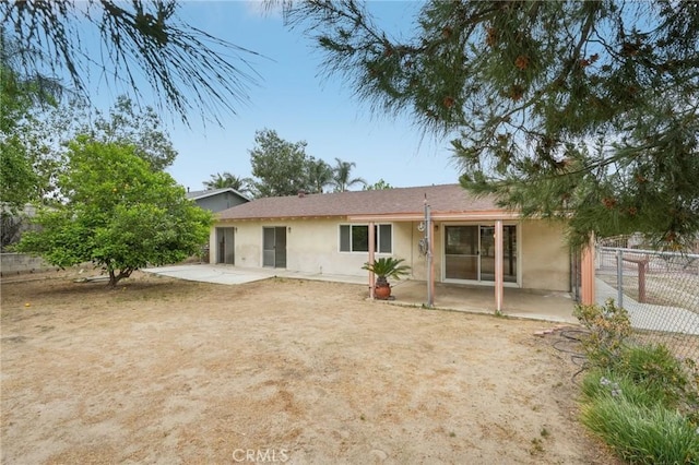 rear view of property featuring stucco siding, fence, and a patio area