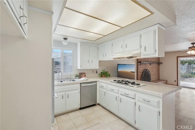 kitchen featuring white gas stovetop, dishwasher, a sink, tile countertops, and a peninsula