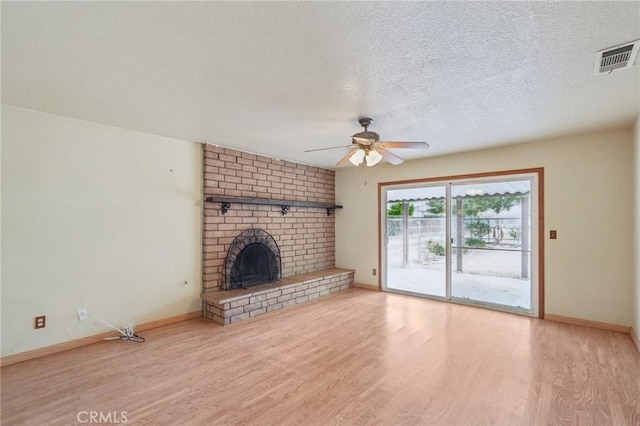unfurnished living room featuring wood finished floors, a ceiling fan, visible vents, and a brick fireplace