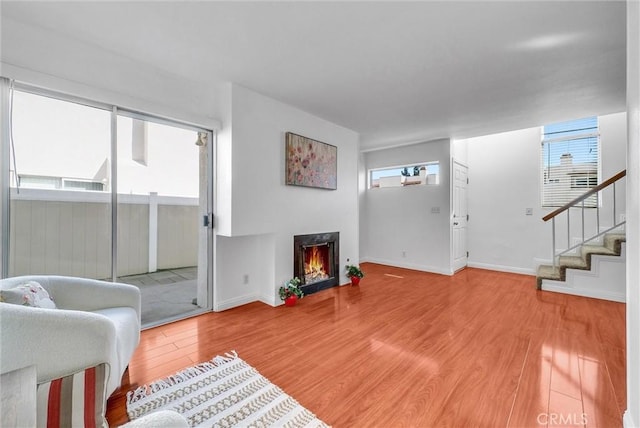 living area featuring stairway, a lit fireplace, baseboards, and wood finished floors
