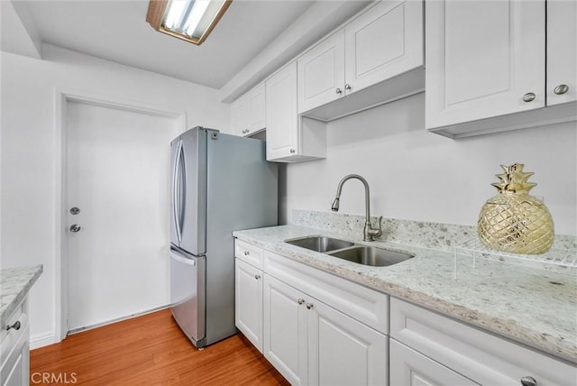 kitchen with a sink, freestanding refrigerator, white cabinetry, wood finished floors, and light stone countertops