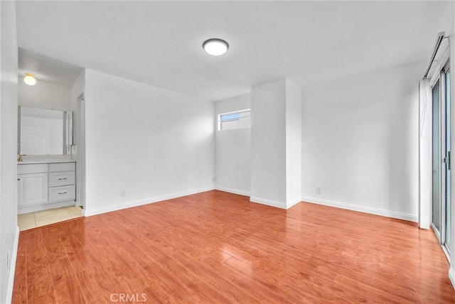 unfurnished bedroom with light wood finished floors, ensuite bathroom, and baseboards