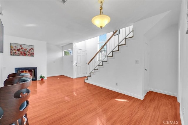 living room with baseboards, wood finished floors, a glass covered fireplace, and stairs