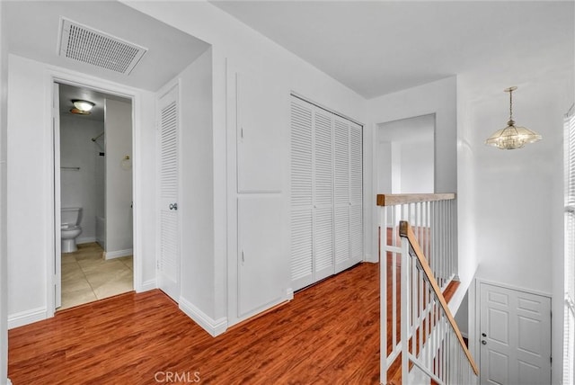 hall with wood finished floors, visible vents, baseboards, and an upstairs landing