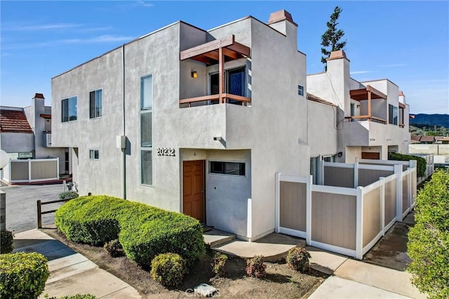 view of front of home with a chimney, stucco siding, fence, and a balcony