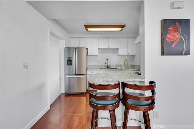 kitchen with baseboards, stainless steel fridge, a sink, white cabinetry, and a breakfast bar area
