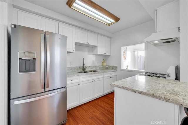 kitchen with ventilation hood, white cabinets, wood finished floors, a sink, and stainless steel fridge