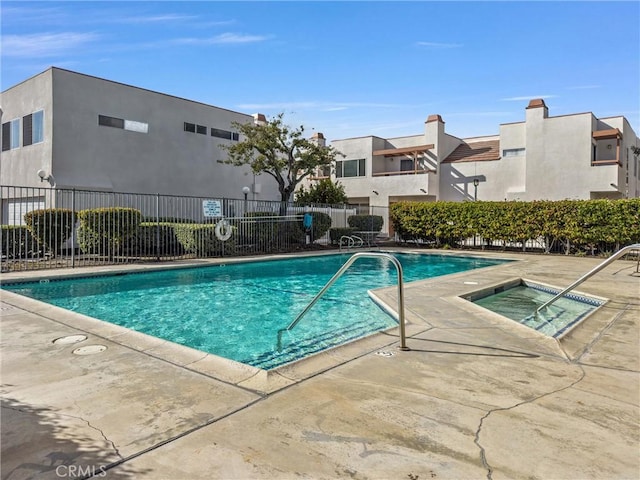 community pool with a patio area, fence, and a hot tub