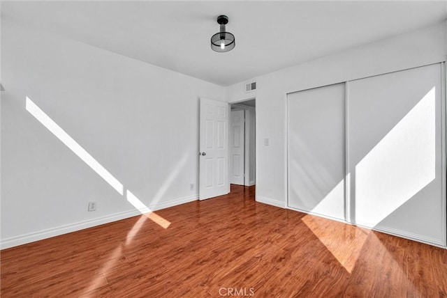 unfurnished bedroom featuring visible vents, a closet, baseboards, and wood finished floors