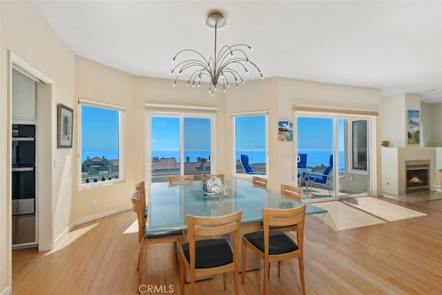 dining room featuring a lit fireplace, baseboards, an inviting chandelier, and wood finished floors