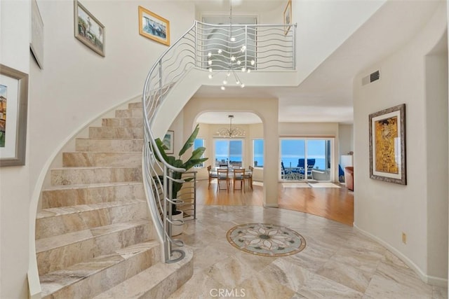 foyer entrance featuring visible vents, stairs, a high ceiling, a chandelier, and arched walkways