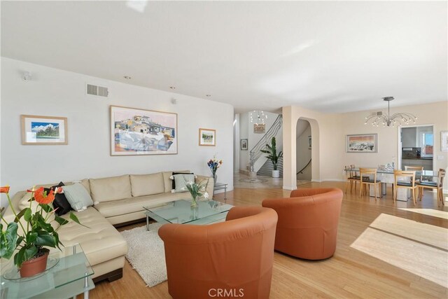 living area with visible vents, arched walkways, wood finished floors, an inviting chandelier, and stairs