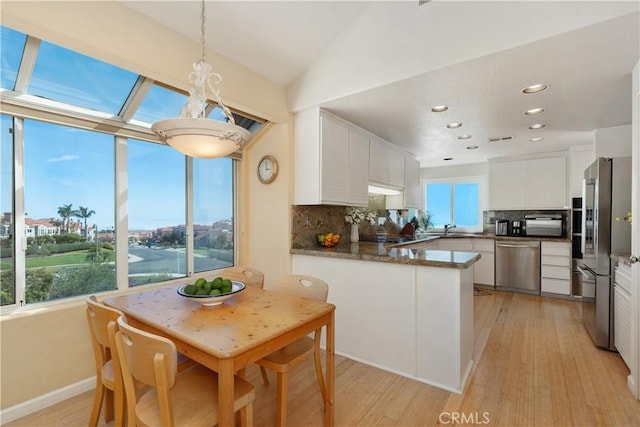 kitchen featuring appliances with stainless steel finishes, tasteful backsplash, a peninsula, light wood finished floors, and white cabinetry