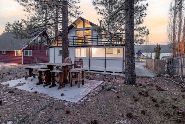 back of house at dusk featuring a patio, a balcony, and fence
