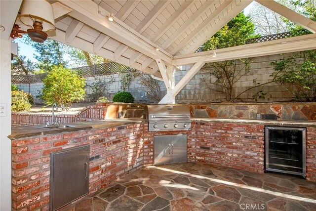 view of patio featuring a sink, wine cooler, grilling area, fence, and an outdoor kitchen