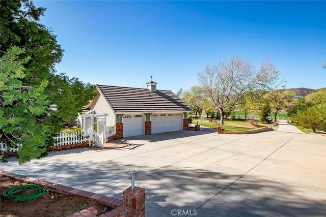 view of side of home with a garage, a tile roof, fence, stucco siding, and driveway