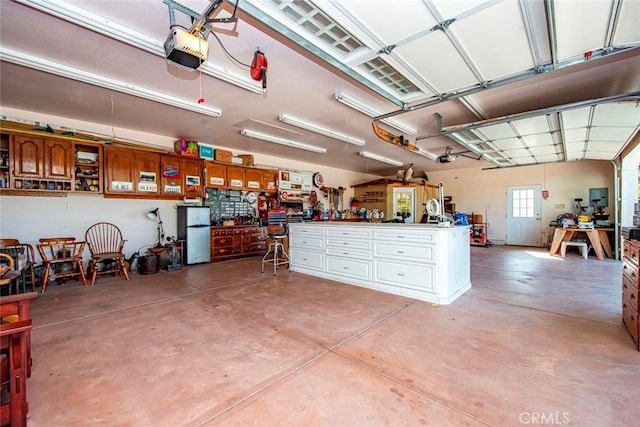 garage featuring a garage door opener, freestanding refrigerator, and a workshop area