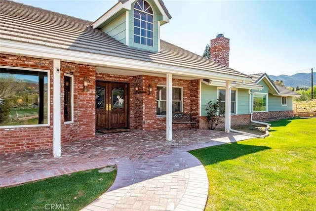 property entrance featuring a mountain view, a yard, a chimney, brick siding, and french doors