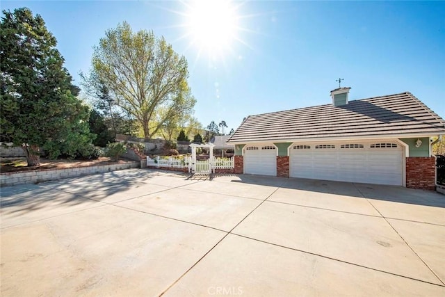 view of property exterior featuring a gate, driveway, brick siding, a garage, and fence