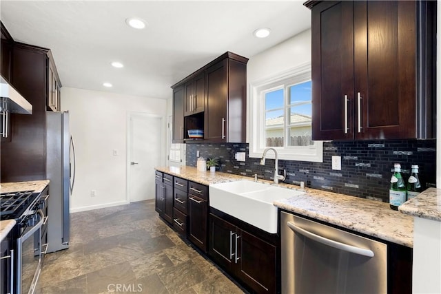 kitchen with baseboards, light stone counters, a sink, backsplash, and stainless steel appliances