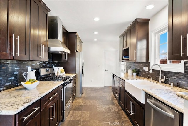 kitchen with dark brown cabinets, light stone countertops, baseboards, wall chimney exhaust hood, and appliances with stainless steel finishes