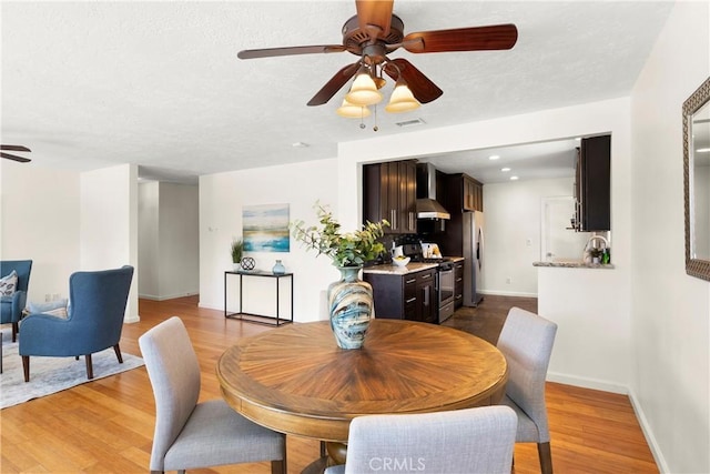 dining space featuring a ceiling fan, a textured ceiling, visible vents, wood finished floors, and baseboards