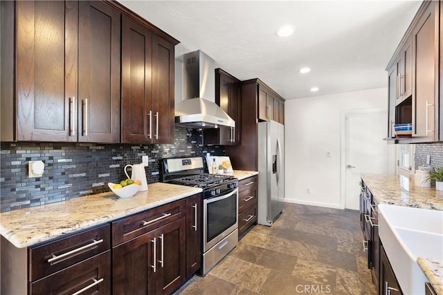 kitchen featuring wall chimney range hood, dark brown cabinetry, appliances with stainless steel finishes, a sink, and backsplash