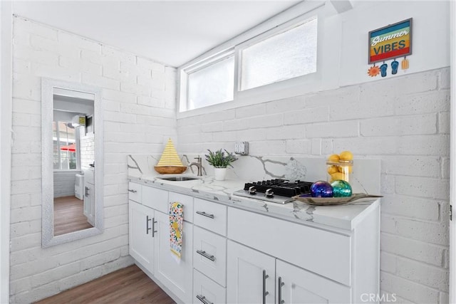 kitchen with light stone counters, white cabinetry, wood finished floors, and a sink