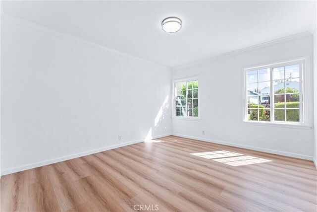 empty room with light wood-type flooring, baseboards, and ornamental molding