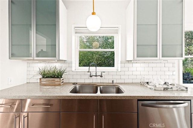 kitchen with a sink, a healthy amount of sunlight, light stone countertops, backsplash, and stainless steel dishwasher