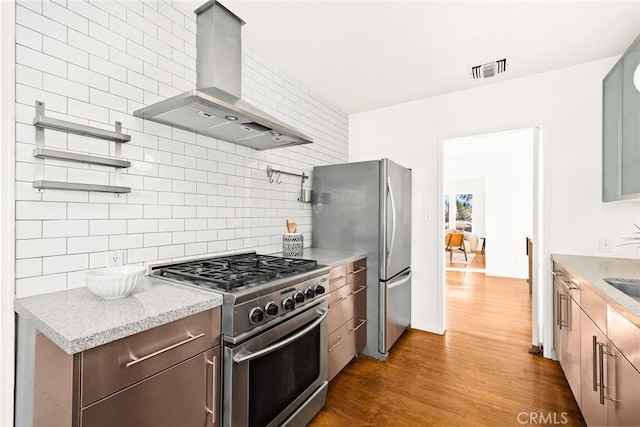 kitchen featuring dark wood-style flooring, wall chimney range hood, light stone countertops, decorative backsplash, and appliances with stainless steel finishes