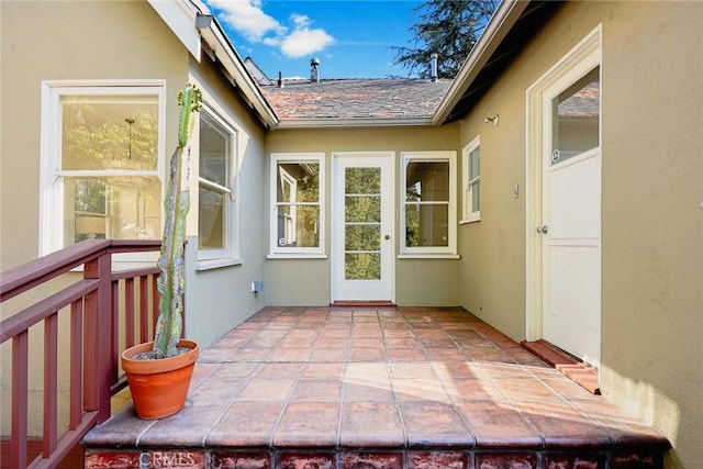 entrance to property with a patio, stucco siding, and roof with shingles