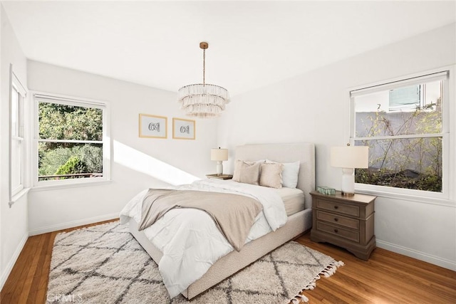 bedroom with baseboards, multiple windows, an inviting chandelier, and wood finished floors