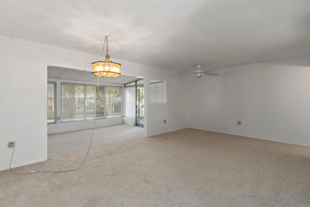 carpeted empty room featuring ceiling fan with notable chandelier and baseboards
