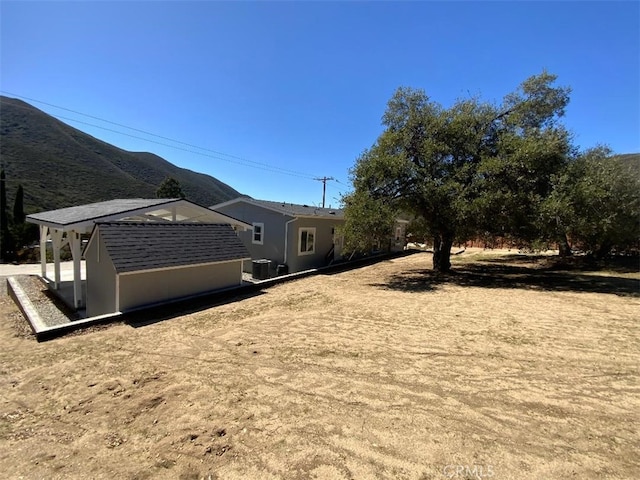view of yard featuring an outbuilding, a mountain view, a storage shed, and central air condition unit